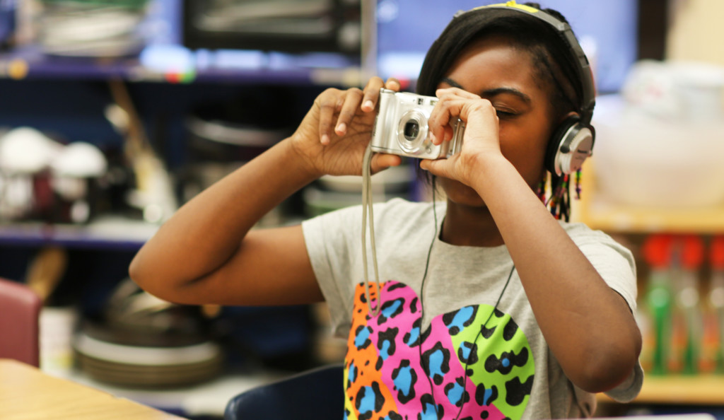 Girl with headphones on is holding a camera up to her face.