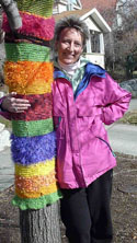 A photo of Sheryl Gillilan embracing a post wrapped in colorful graffiti knitting