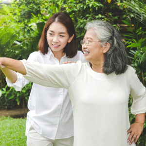 An older adult woman striking a creative movement pose with the guidance of a younger adult.