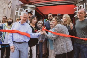 A ribbon-cutting ceremony with a large group of smiling people in front of a building's open glass doors.