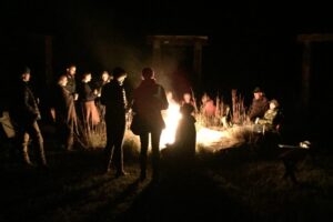 A group of people gather around a bonfire at night. 