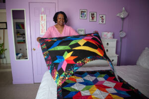 A woman placing a bright, rainbow-colored and star-patterned quilt top onto another similar quilt top.