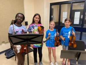 Young children cheerfully posing with violins in a classroom setup.